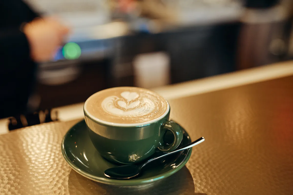 Kapučino z latte artom v zelenem lončku.